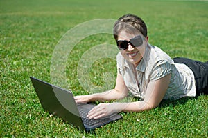 Woman working on laptop in summer outdoor, lie on your belly on green grass meadow, happy people, city park