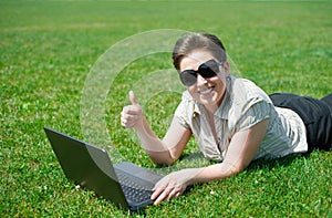 Woman working on laptop in summer outdoor, lie on your belly on green grass meadow, show best gesture, happy people, city park