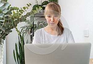Woman working on laptop surrounded by plants and flowers on balcony at daytime