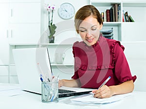 Woman working with laptop and taking notes