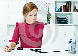 Woman working with laptop and taking notes
