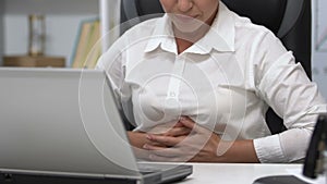 Woman working on laptop touching belly, gastritis problem, irregular nutrition