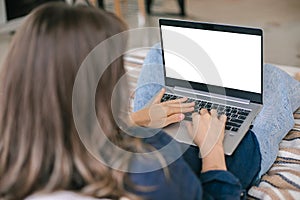 Woman working on mockup laptop while sitting on bed at her cozy home. Female freelance typing on keyboard