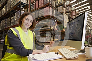 Woman working in the office of a warehouse looks to camera