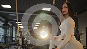 A woman working out her thigh with a dumbbell in a dark gym room.