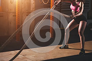 Woman working out in training gym doing cross fit exercise with battle ropes