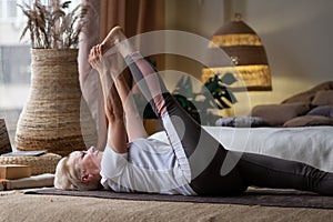 Woman working out, warming up using yogic belt, lying in yoga Supta Padangushthasana, One Leg Lift exercise