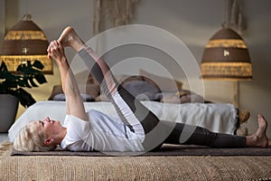 Woman working out, warming up using yogic belt, lying in yoga Supta Padangushthasana, One Leg Lift exercise