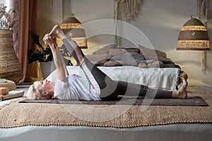 Woman working out, warming up using yogic belt, lying in yoga Supta Padangushthasana, One Leg Lift exercise