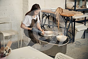 Woman working on pottery wheel in workshop making clay bowl