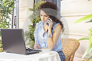 Woman working remotely with laptop and phone in cafe. Happy businesswoman calling on mobile phone and taking photo