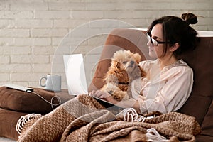 The woman is working remotely. Women with the dog working using a laptop at home.