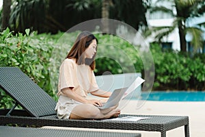 A woman working at the swimming pool with her laptop computer holding paperwork in her hand. It is imperative for young Asian
