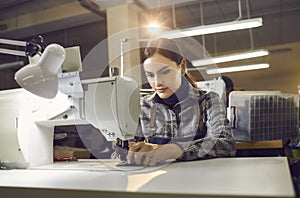 Woman working at table with industrial sewing machine at shoe or clothing factory
