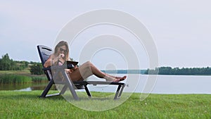 Woman working on a tablet computer traveling the world on vacation, sunbathing on the beach near the lake