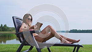 Woman working on a tablet computer traveling the world on vacation, sunbathing on the beach near the lake