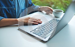 A woman working and touching on laptop computer touchpad while drinking coffee