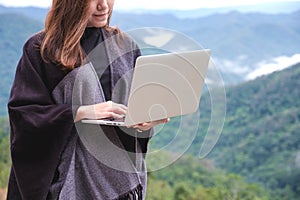 A woman working and typing on laptop with green mountains on foggy day with blue sky background