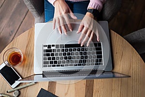 Woman is working by using a laptop computer on wooden table. Hands typing on a keyboard.