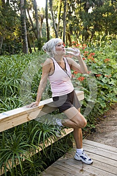 Woman in workout clothes drinking water in park