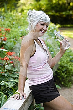 Woman in workout clothes drinking water in park