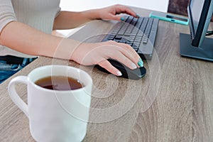 A woman works on a computer from home. Cropped image of businesswoman using computer while having tea at desk Remote work..