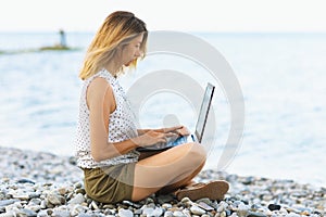 A woman works at a computer on the seashore, combines rest and work