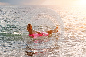 Woman works on laptop in sea. Freelancer, blond woman in sunglases floating on an inflatable big pink donut with a