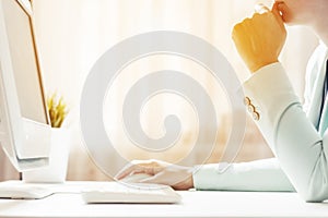 A woman works in an office. Looks at the computer screen. Sunlight in the window. Closeup