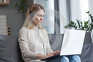 The woman works remotely at home as an online consultant, uses a headset and laptop for a video call