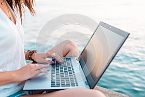 A woman works remotely on a laptop. Hands close-up. Sea in the background. The concept of freelancing