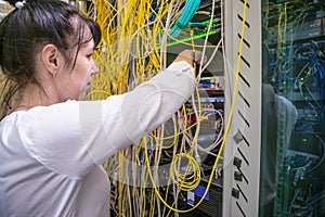 The woman works in the server room of the data center. The girl switches fiber-optic Internet wires in a rack with powerful