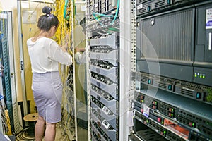 A woman works in a server room. The girl switches the wires in the routers of the Internet provider. The specialist works in the