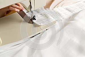 A woman works on a sewing machine. seamstress sews white curtains, close up view.