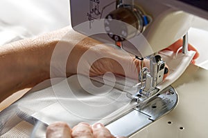 A woman works on a sewing machine. seamstress sews white curtains, close up view.