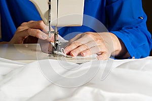 A woman works on a sewing machine. seamstress sews white curtains, close up view.