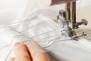 A woman works on a sewing machine. seamstress sews white curtains, close up view.
