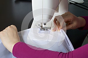 A woman works on a sewing machine. She sews the curtains on the window