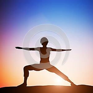 Woman in worrior yoga pose meditating at sunset. Zen