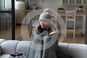 Woman wrapped in blanket making phone call, cold at home