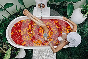 Woman relaxing in outdoor bath with flowers in Bali spa hotel