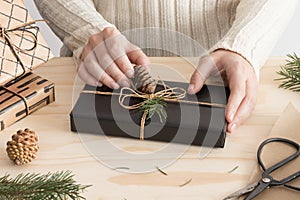Woman wrapping a black christmas gift on a wooden table with christmas decoration