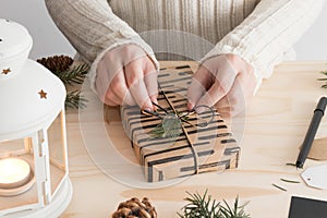 Woman wrapping a black christmas gift on a wooden table with christmas decoration