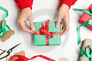 Woman wrapping Christmas gift at white wooden table