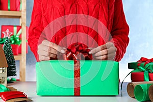 Woman wrapping Christmas gift at white wooden table indoors