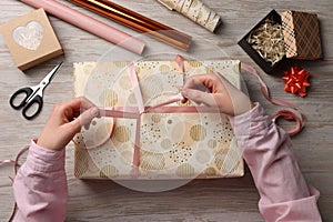 Woman wrapping Christmas gift at white wooden table, top view