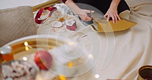 Woman Wrapping Christmas Present By Fireplace At Home