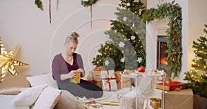 Woman Wrapping Christmas Present By Fireplace At Home