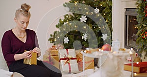 Woman wrapping Christmas present by fireplace at home