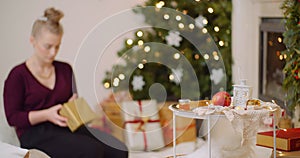 Woman wrapping Christmas present by fireplace at home